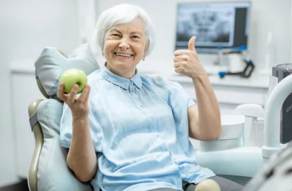a woman in the dentist's chair holding an apple and the thumb up