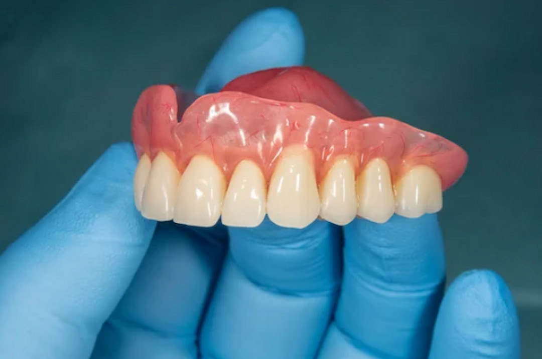 a person with rubber gloves holding dentures