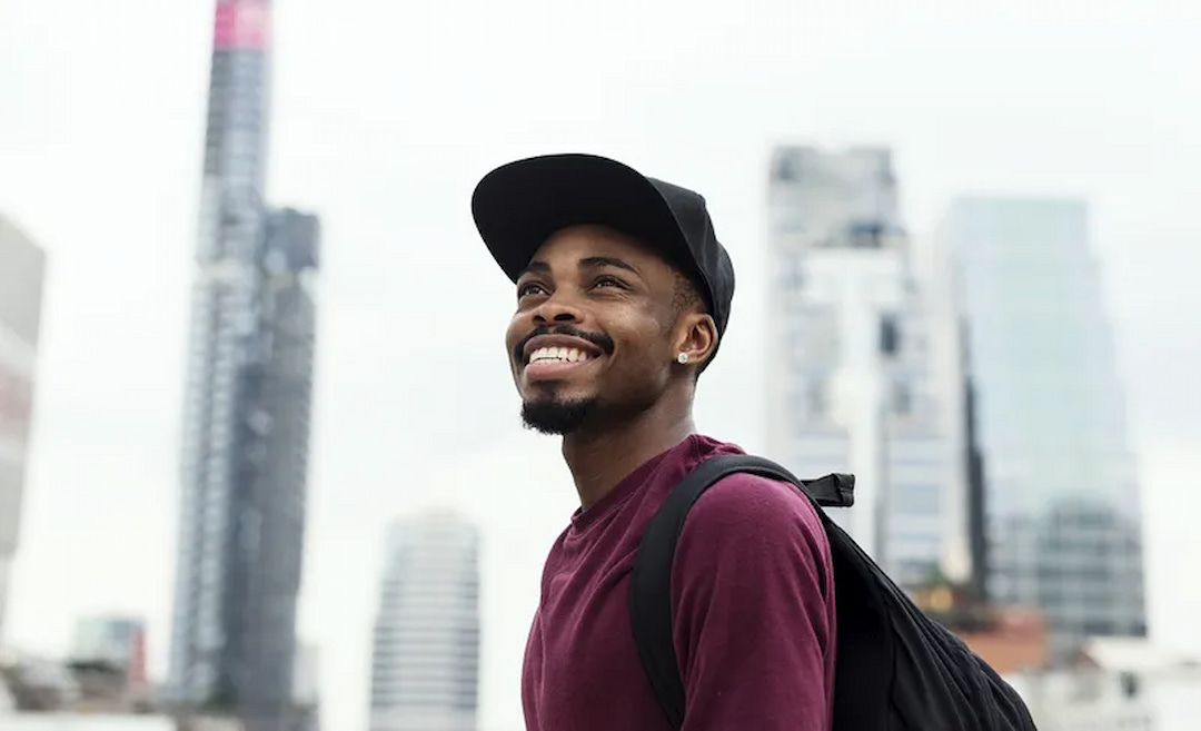a young smiling man with a cap and a backpack