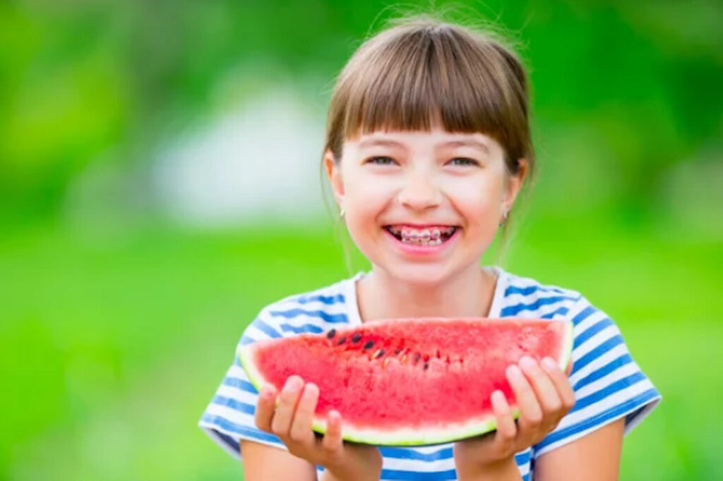 a smiling little girl with braces holding a slice of watermelon