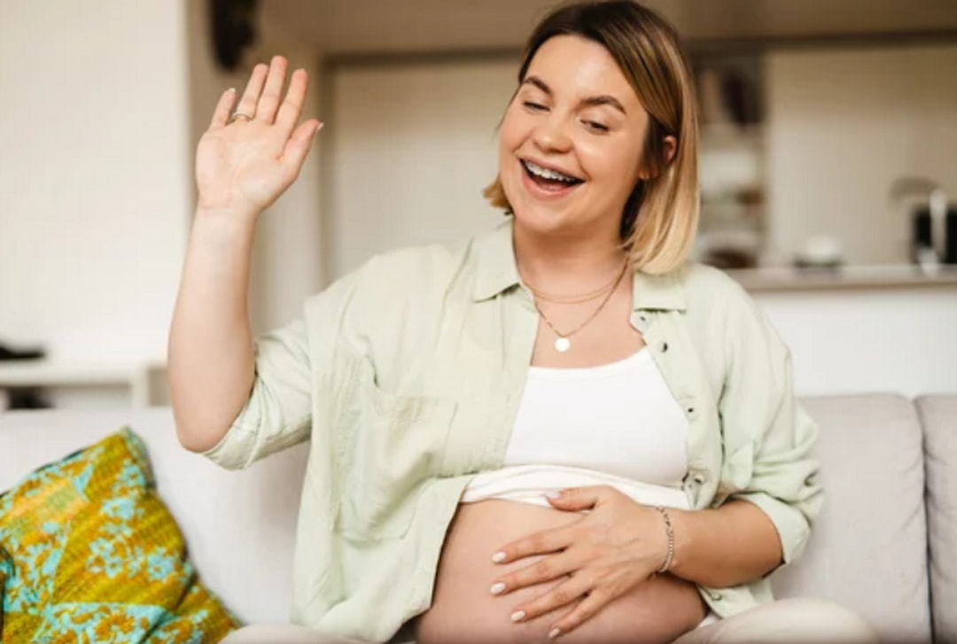 a smiling pregnant woman waving with her hand