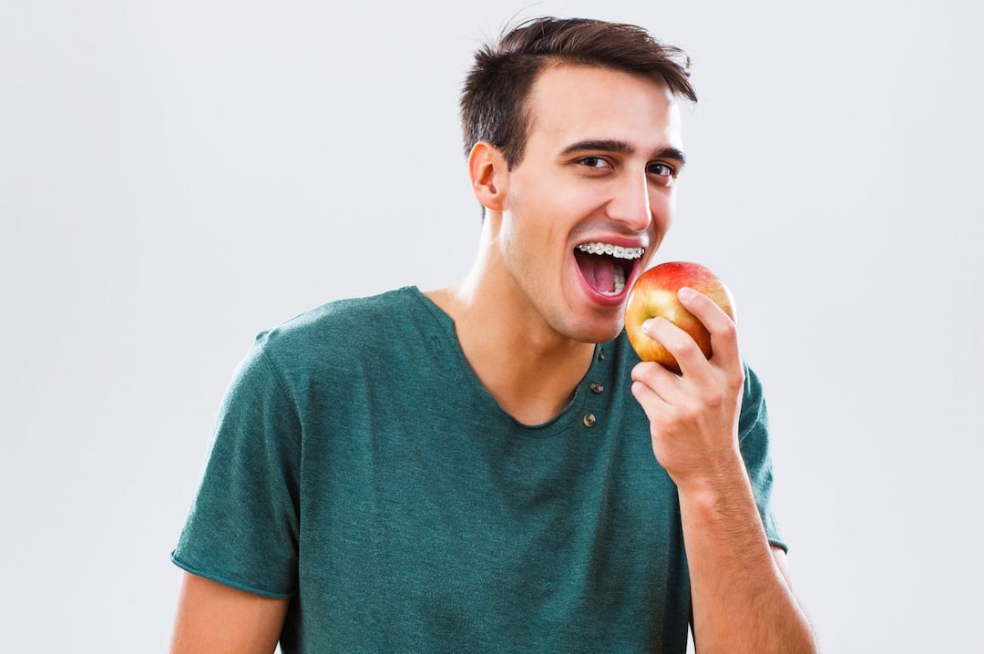 young man with braces eating an apple
